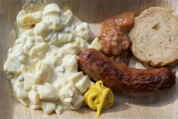 Жареная колбаса с картофельным салатом, горчицей и хлебом на бамбуковой тарелке, фаст-фуд на уличный фестиваль, вид сверху — стоковое фото
