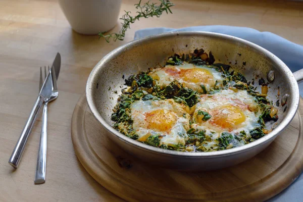 Τηγάνι σπανάκι με τηγανητό αυγό και μπαχαρικά, πλούσιο σε πρωτεΐνες χορτοφαγικό πιάτο για χαμηλή διατροφή υδατανθράκων σε μια ρουστίκ ξύλινη σανίδα — Φωτογραφία Αρχείου