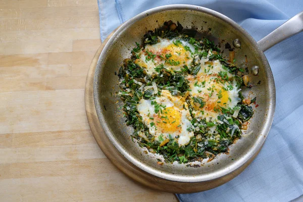 Poêle aux épinards et œufs frits, épices et garniture aux herbes, plat riche en protéines pour une alimentation faible en glucides sur une table en bois, espace pour copier, vue de dessus grand angle d'en haut — Photo