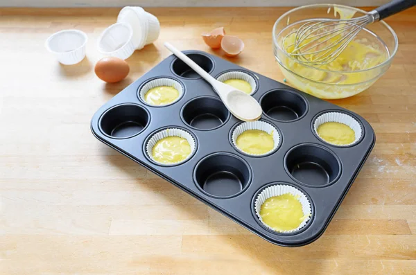 Muffinsburk, delvis fylld med papperskoppar och deg för muffinsbakning på ett köksbord av trä, kopieringsutrymme — Stockfoto