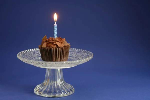 Magdalena de cumpleaños con chocolate y una vela encendida en un tazón de vidrio, fondo azul con gran espacio de copia — Foto de Stock