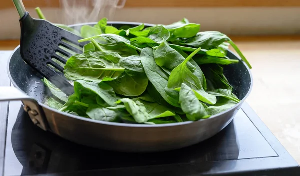 Friggere gli spinaci freschi in una padella sul fuoco, una cucina sana a casa concetto — Foto Stock
