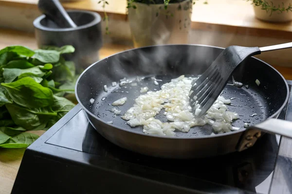 As cebolas fritam-se com muito vapor em uma panela preta, cozinha e conceito de cozinha — Fotografia de Stock