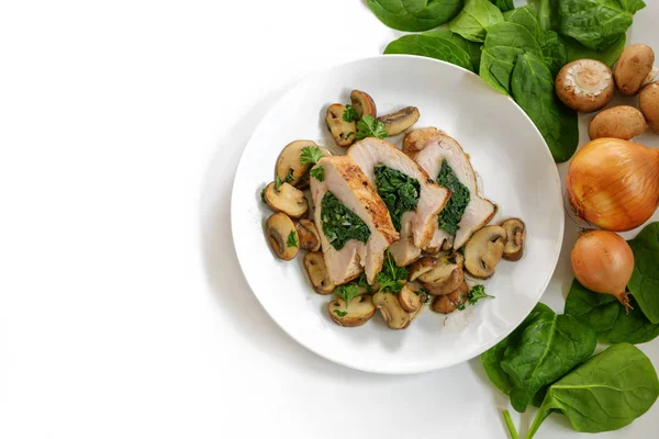 Chicken breast fillet with spinach filling, mushrooms, onion and parsley garnish on a plate, some raw ingredients, white background with large copy space — Stock Photo, Image