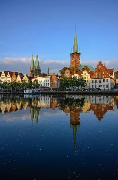 Paisaje urbano del casco antiguo histórico de Luebeck en Alemania con reflejo en el río Trave, iluminado por el sol poniente al final de la tarde, agua azul oscura y cielo, espacio para copiar — Foto de Stock