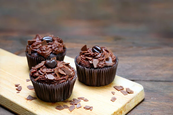 Cupcakes de chocolate con crema de manteca de cacao en una tabla de cortar y una mesa de madera oscura, espacio para copiar —  Fotos de Stock