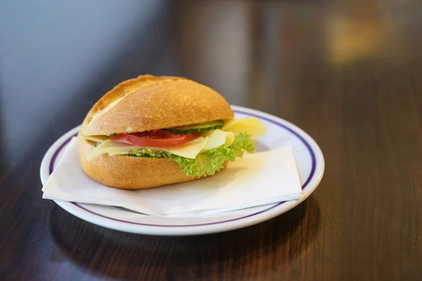 Bułka chlebowa z serem, pomidorem i sałatą serwowana jako śniadanie lub szybka przekąska na talerzu na ciemnym drewnianym stole, przestrzeń do kopiowania — Zdjęcie stockowe