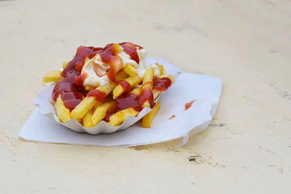 Batatas fritas com maionese e ketchup em um prato de papelão ao ar livre em uma mesa de madeira pintada, fast food insalubre, na alemanha chamado pommes vermelho branco, espaço de cópia — Fotografia de Stock