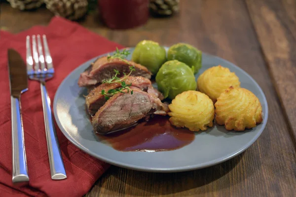 Petto d'anatra grigliato con germoglio di Bruxelles, patate duchessa e salsa, come cena di Natale festiva, tovagliolo rosso su un tavolo di legno scuro — Foto Stock