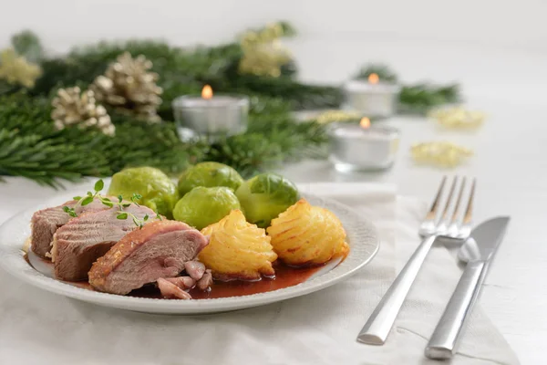 Filetto di petto d'anatra con patate duchessa e germoglio di Bruxelles, cena festiva servita con candele, rami di abete e decorazione natalizia su un tavolo di legno bianco — Foto Stock