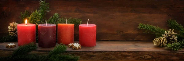 First Advent, four red candles, one of them is burning, fir branches and Christmas decoration on dark rustic wood, wide panoramic format with copy space — Stock Photo, Image