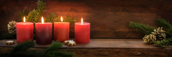 在修道院的第四个星期日，四支燃烧的红烛连成一排，冷杉枝条和圣诞装饰品点缀在漆黑的乡村木柴上，全景版面宽阔，有复制空间 — 图库照片