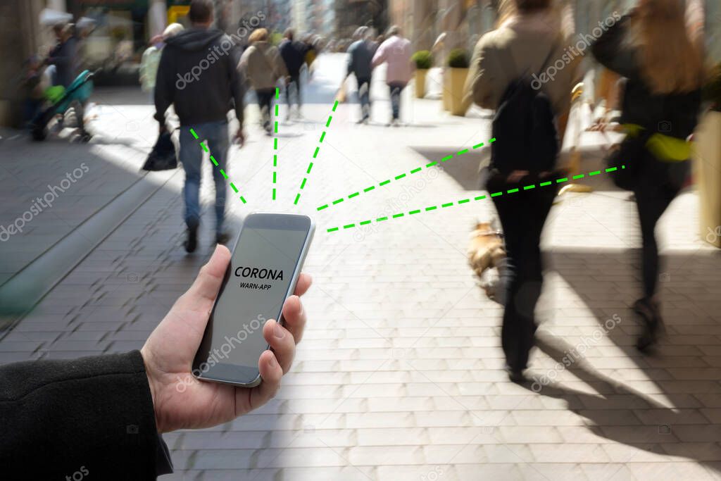 Smart phone with Corona Warn App, the contact tracking or tracing application against Covid 19 pandemic is connecting other phones from moving people in the city to analyze the risk of infection, copy space, blur motion, selected focu
