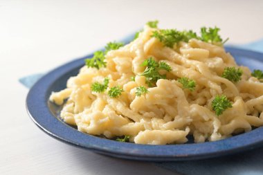Mavi bir tabak ve beyaz bir masa üzerinde maydanozlu spaetzle, Schwaben, Güney Almanya ve Avusturya 'da tipik bir yemek, seçilmiş odak noktası, çok dar bir alan derinliği