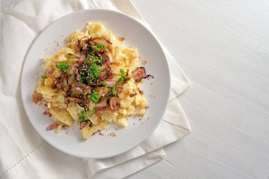 Spaetzle, peynirli ev yapımı yumurtalı şehriye, kızarmış pastırma, soğan ve ekmek kırıntıları, maydanozlu garnitür ile beyaz boyanmış ahşap masa, Güney Almanya ve Avusturya 'da geleneksel yemek, kopya alanı, yukarıdan yüksek açı, seçilmiş odak noktası