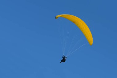 Sarı planörlü paraglider pilotu açık mavi gökyüzünde uçuyor, eğlence amaçlı ve rekabetçi macera sporu, kopyalama alanı