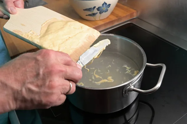 調理スパエッツェル 男の手は 木製の板から沸騰した水に自家製の卵パスタ生地をスクレープしている Schwaben 南ドイツとオーストリアの典型的な料理 選択されたフォーカス フィールドの狭い深さ — ストック写真