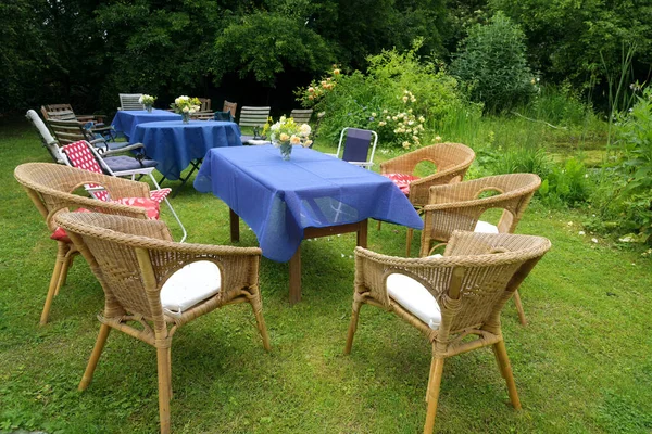 田舎の庭でテーブル 青いテーブルクロス 多くの異なる椅子を備えたカジュアルな夏のパーティーのために設定されています — ストック写真