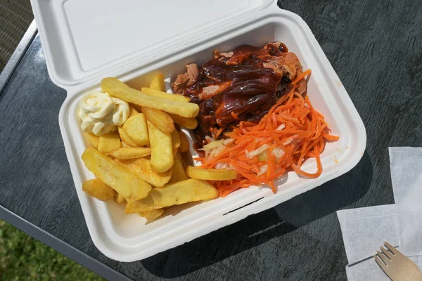 Fast food to go in a box with pulled pork, coleslaw and carrot salad, french fries, barbecue sauce and mayonnaise, high angle view from above,