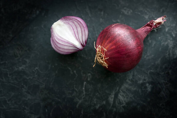 Red onion whole and halved, healthy and spicy vegetable on a dark slate background with copy space, selected focus