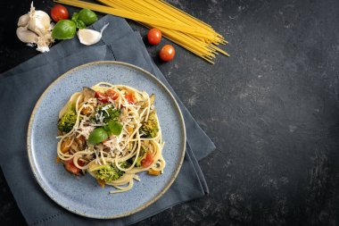 Taze sebzeli spagetti makarna ve parmesan peyniri, sağlıklı vejetaryen yemeği ve mavi tabakta bulunan malzemeler ve fotokopi alanı olan koyu gri kırsal arka plan, yukarıdan yüksek açılı görüş, seçilmiş odak noktası.