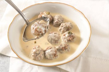 Ladle is liftiting a meatball from a bowl with koenigsberger klops, which are boiled beef balls in a white bechamel sauce with capers, traditional Polish and German dish, selected focus, narrow depth of field clipart