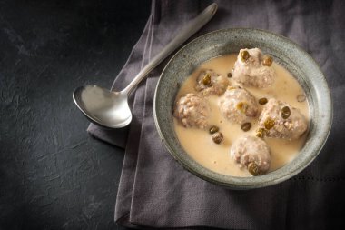 Boiled meatballs in a white bechamel sauce with capers, called Koenigsberger Klopse, traditional Polish and German dish in bowl on a dark gray background with copy space, view from above, selected focus clipart