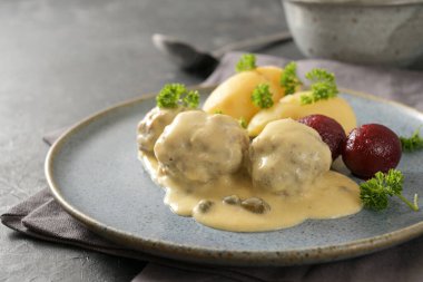 Koenigsberger Klopse or meatballs in a white bechamel sauce with capers, potatoes and beetroot served on a gray blue plate, traditional Polish and German dish, copy space, selected focus, narrow depth of field clipart