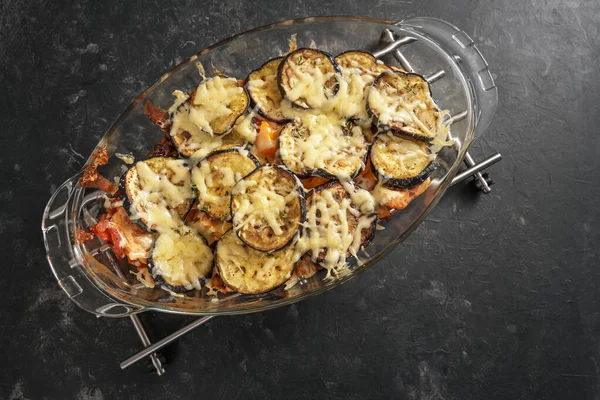ナスと野菜グラタン トマトとベルペッパー暗い石の背景にガラス鍋料理でチーズで焼きます コピースペース 上から高い角度ビュー — ストック写真