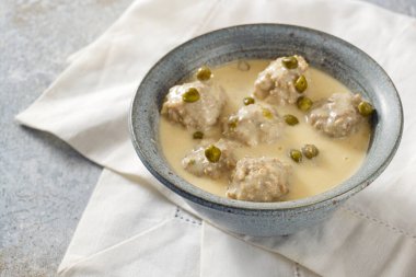 Koenigsberger Klopse or boiled meatballs in a white bechamel sauce with capers, traditional Polish and German dish in a gray bowl on a white napkin, selected focus, narrow depth of field clipart