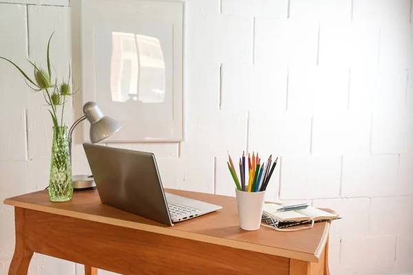 Small wooden home office desk from behind  with laptop and tools against a rough white wall, copy space, selected focus, narrow depth of field