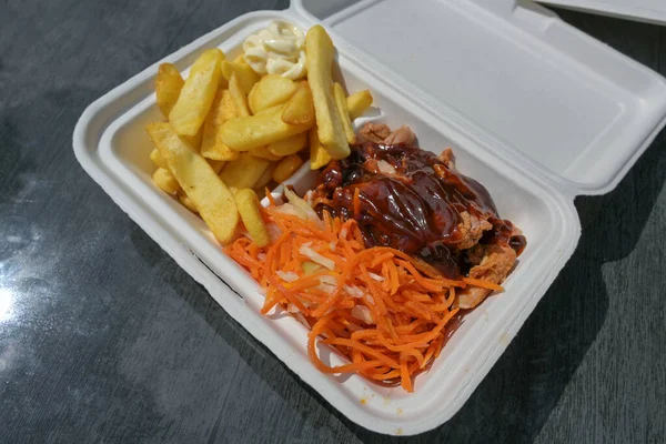 Pulled pork in a take away box with barbecue sauce, coleslaw and carrot salad, french fries and mayonnaise fast food on a table in a street restaurant, selected focus, narrow depth of field