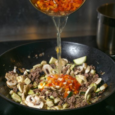 Kızarmış et ve sebzeler, siyah bir tencerede kızartılmış et ve sebzeler, dolma biber çorbası, koyu arka plan, hareket bulanıklığı, seçilmiş odak, dar alan derinliği ile kaplanır.