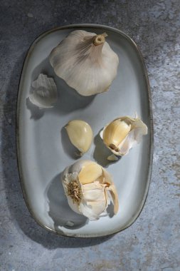 Mavi gri bir tabakta sarımsak soğanları ve karanfiller ve taş bir arka plan, sağlıklı gıda ve tıbbi bitki, yukarıdan yüksek açı, seçilmiş odak, dar alan derinliği