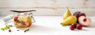 Armutlar, şeftaliler ve kiraz erikleri, taze ve cam bir kavanozda tarçın, nane ve vanilya ile beyaz boyanmış ahşap zemin, panoramik format, kopyalama alanı, seçilmiş odak