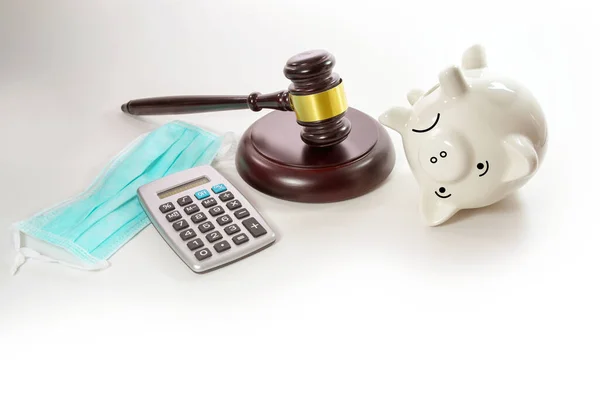 Sad piggy bank is on its back, calculator, surgical mask and threatening judge gavel, reserves are used up during coronavirus pandemic, gray background is fading to white, copy space, selected focus