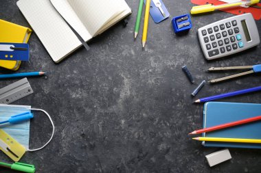 Kırtasiye malzemelerinden çerçeve, aralarında Coronavirus ve covid 19 enfeksiyonuna karşı cerrahi maske, okula geri dönüş ve karanlık arka planda fotokopi alanı olan yeni normal konsept, yukarıdan yüksek açılı görüş.