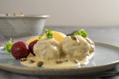 Almanya 'da kapari soslu kaynamış köfteler Koenigsberger Klopse olarak adlandırılır. Gri bir tabakta pancar patatesli ve maydanozlu geleneksel yemek. Fotokopi alanı, seçilmiş odak ve dar alan derinliği ile yakın plan. 
