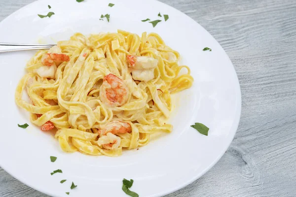 Паста Tagliatelle Креветками Шафрановым Соусом Белой Тарелке Сером Деревянном Столе — стоковое фото