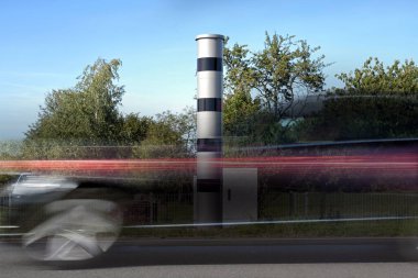 Long time exposure at a speed measuring device and a fast passing car in motion blur, automatic traffic monitoring with light radar and camera to punish speeding with fines or revocation of driving license, copy space clipart
