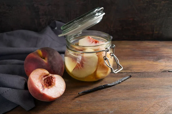 冬に缶詰の果物を持っているバニラとガラス瓶に保存されている桃 青ナプキンと暗い素朴な木 コピースペース 選択された焦点 フィールドの狭い深さ — ストック写真