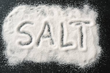 Yazılı Kelime SALT, yukarıdan seçilmiş, yüksek açılı, koyu bir levha üzerine tuz kristalleri döktü