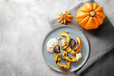 Fırınlanmış balkabağı veya kabak, kırmızı soğan, balzamik soslu feta peyniri ve kekik mavi tabakta ekşi krema ve gri arka plan, fotokopi alanı, yukarıdan yüksek açı görünümü