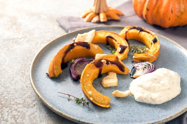 Pumpkin or squash wedges baked with red onions, feta cheese and thyme, also balsamic sauce and a sour cream dip on a gray blue plate, Thanksgiving or Halloween appetizer, copy space, selected focus, narrow depth of field