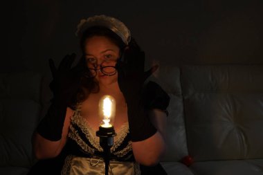 Karanlıkta kırmızı-sıcak bir spiral ile ampul tutan bir kadının portresi. Enerji tasarrufu. Esmer hizmetçi.                          