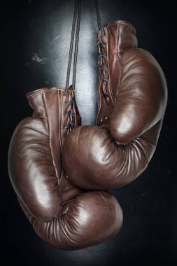 Kahverengi boks eldivenleri siyah arka plandaki bağcıklara asılıyor. Spor malzemeleri. Antrenman. Dövüş. Antrenman.                              