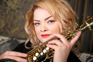 Elinde saksafon olan çekici bir sarışının portresi. Siyah gece elbisesi içinde güzel bir kız. Saçları parlak kırmızı dudaklı genç bir kadın. Yüzünü yaklaştır. Saksafoncu bayan.
