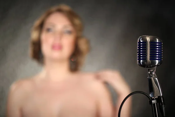 Girl singing in a retro microphone. Recording a clip in the studio of a professional singer. Close up face of singer with microphone on smoky gray background. The singer sings a song on stage.