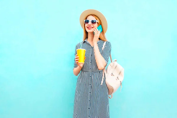 笑顔の女性は スマート フォンで話しているファッションのバックパックをカラフルな青の背景にジュースのカップを保持しています — ストック写真