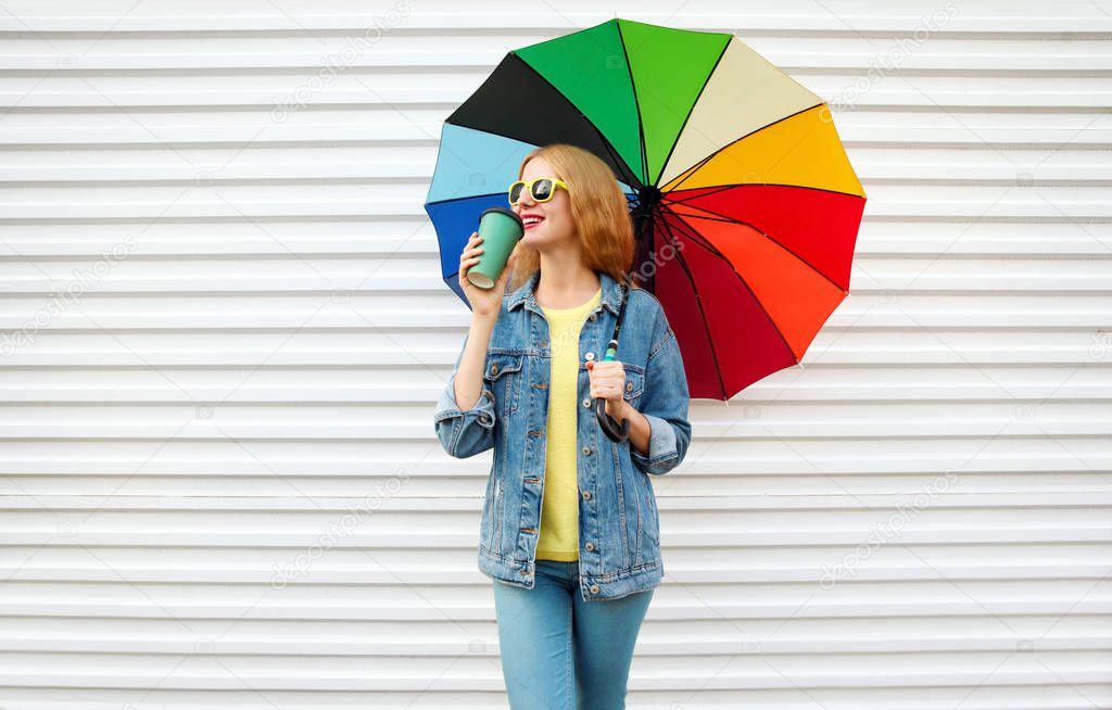 Happy smiling woman drinks coffee, holds colorful umbrella on white wall background